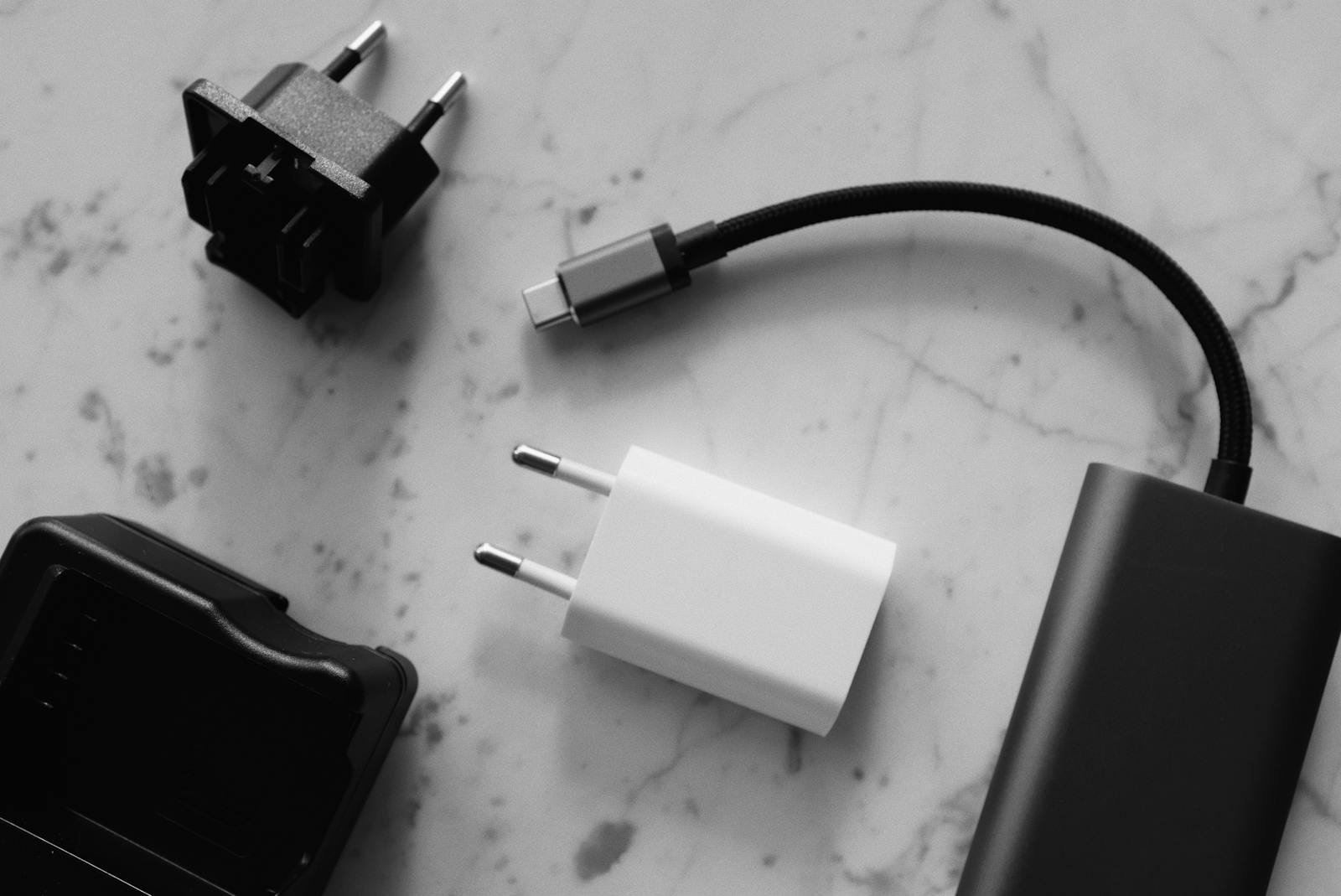 Composition of various modern charging units with adapter and small black external battery with short cable placed on white marble table
